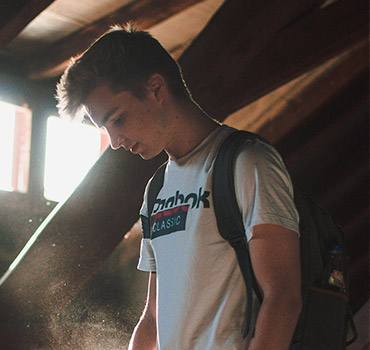 male teen standing in a dark basement with sunlight shining through windows