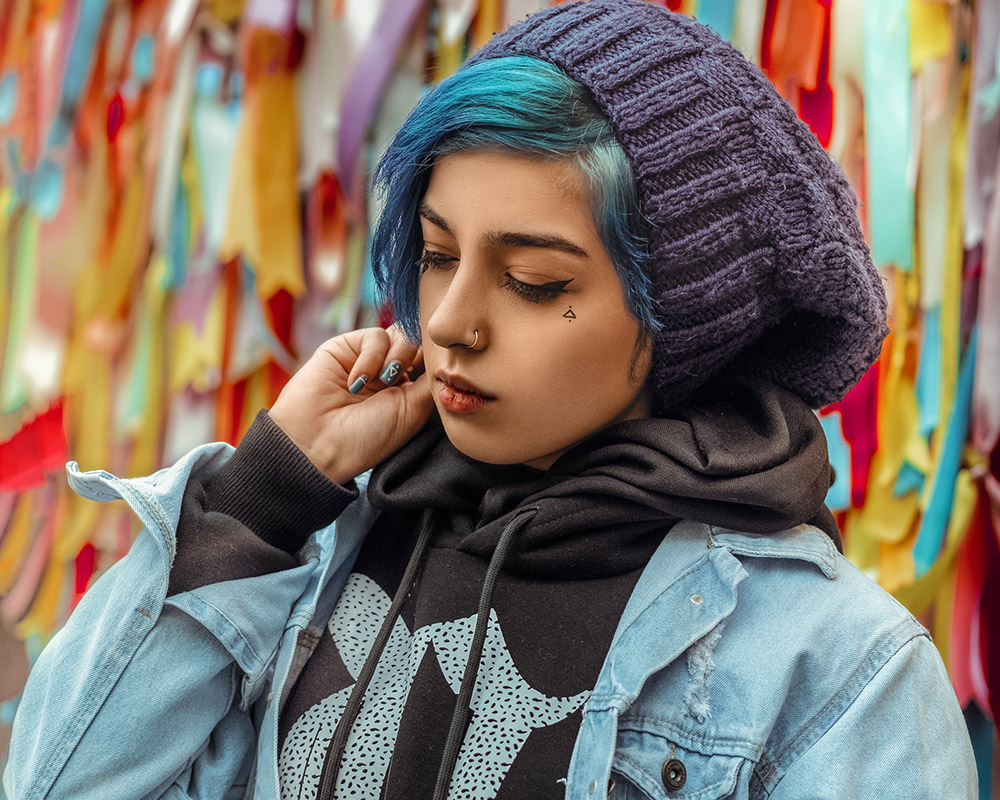 Young woman with blue hair standing in front of a colorful wall