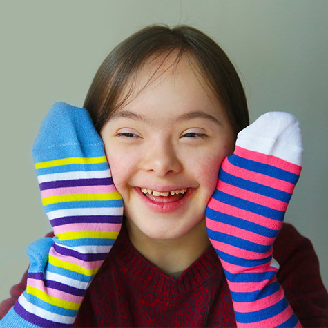 special needs girl smiling with a brightly colored sock on each hand