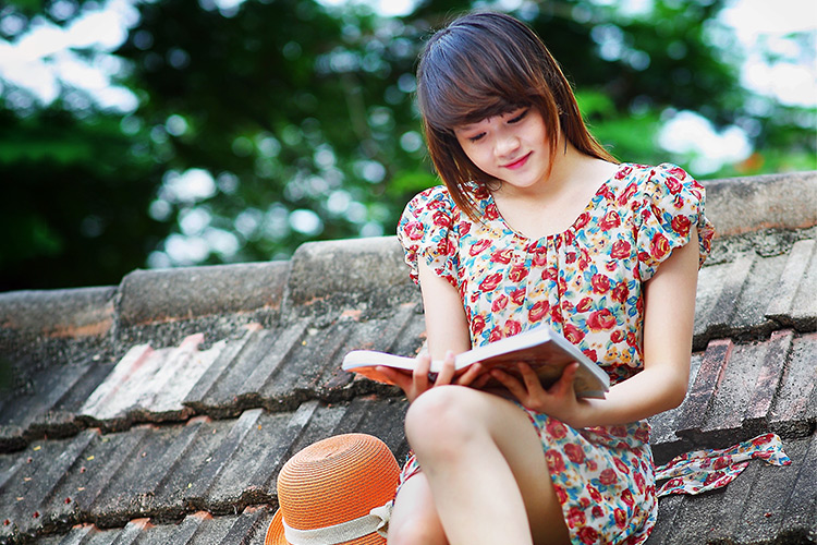 Young woman sitting on the roof of a house in the woods reading a book