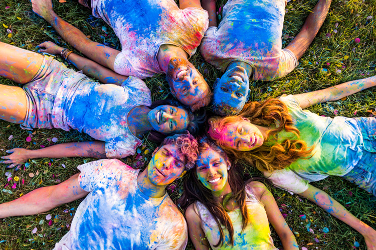 Group of young men and women, laying in a circle, covered in colorful dust